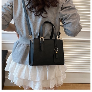 Detail of a chic black leather tote bag with gold hardware worn as a crossbody by a model