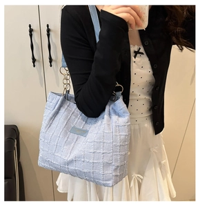 Detail of light blue textured tote bag with gold chain strap and leather patch