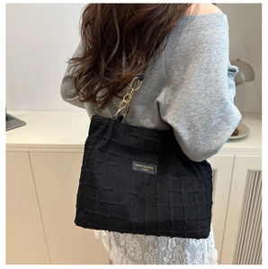 Detail of black textured tote bag featuring a gold chain strap and brand name plaque