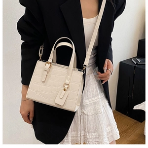 Detail of cream crocodile embossed leather handbag with gold hardware on a model