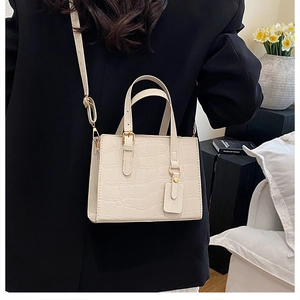 Detail view of cream crocodile-embossed leather handbag worn with a chic black blazer