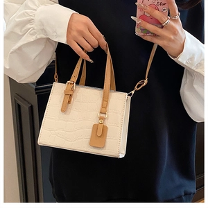 Detail of white crocodile embossed texture on a crossbody bag with brown handles