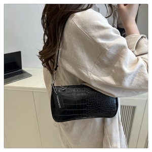 Detail of black crocodile texture baguette bag featuring a fashion tag on shoulder strap