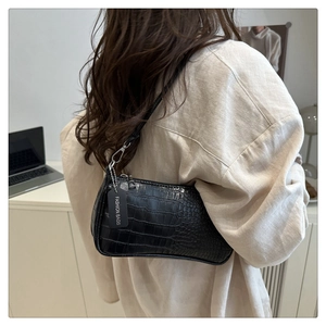Detail of black crocodile embossed baguette bag worn by model in minimalist setting