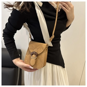 Détail d'un petit sac bandoulière en daim marron avec boucle vintage sur un mannequin