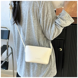 Détail du petit sac bandoulière blanc en cuir grainé avec logo Fashion porté par un modèle