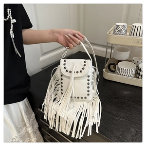 Detalle de mini bolso blanco con flecos y remaches metálicos en textura de piel