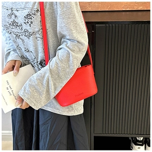 Détail d'un petit sac bandoulière rouge texture litchi porté sur un pull gris chiné