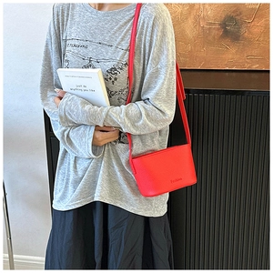 Détail d'un petit sac bandoulière rouge vif en cuir texturé porté par un mannequin en extérieur
