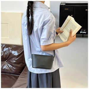 Gros plan d'un petit sac bandoulière noir grainé porté par un mannequin en style décontracté