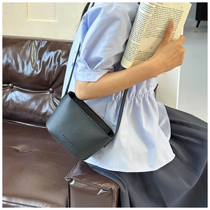 Détail d'un sac bandoulière en cuir grainé noir avec logo embossé fashion sur canapé