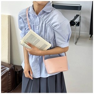 Détail du sac à bandoulière rose motif litchi avec logo Fashion sur chemise bleue