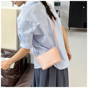 Gros plan du sac bandoulière rose à motif litchi avec logo Fashion et lanière