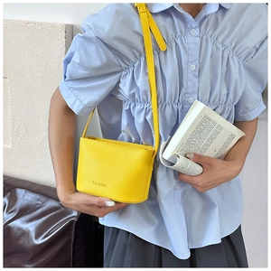 Détail d'un petit sac à bandoulière jaune vif avec texture litchi et lettrage embossé