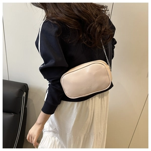 Gros plan d'un sac bandoulière en cuir beige avec chaîne argentée porté par un mannequin