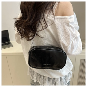 Détail d'un sac bandoulière en cuir noir brillant avec chaîne argentée et logo gravé
