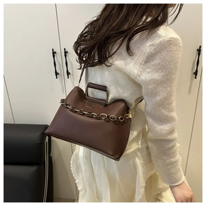Detailed view of brown leather handbag featuring metal handles and decorative chain straps