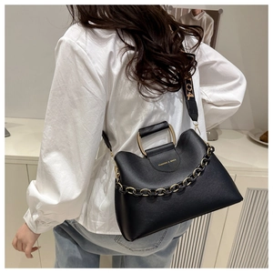 Detail of black matte bucket bag with golden chain and printed strap shown on model