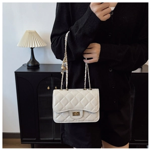 Détail du sac matelassé beige avec bandoulière en chaîne dorée et breloque boule