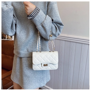 Close-up of white quilted leather texture and gold metal twist lock on a flap chain bag