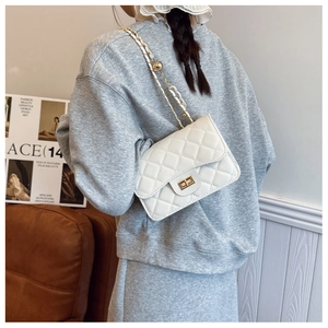 On-body view of white quilted crossbody bag with gold chain strap and metal ball