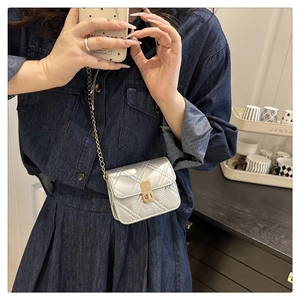 Detail of silver quilted crossbody bag with gold metallic lock and chain strap on model
