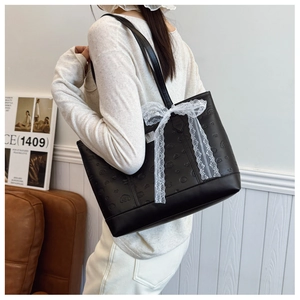 Détail du sac cabas noir avec motifs gaufrés, nœud en dentelle blanche et doubles anses