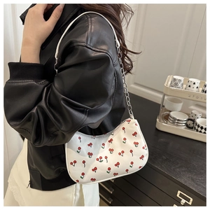 Detail of white cherry print baguette bag with silver chain strap on a black leather jacket