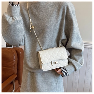Detailed view of a white quilted crossbody bag featuring a gold chain strap and turn-lock