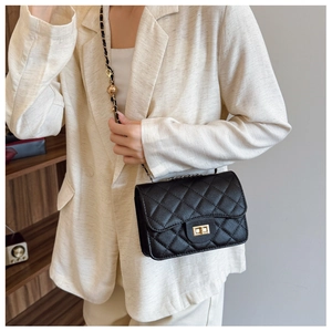Detail of black quilted leather crossbody bag featuring gold ball chain and metal lock