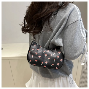 Close-up of black shoulder bag with red cherry prints and silver chain strap on a model