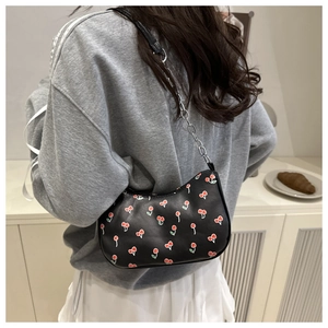 Model wearing a black leather underarm bag with cherry print and silver chain strap