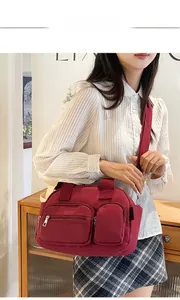 Deep red nylon shoulder bag shown worn cross-body highlighting durable multi-pocket design