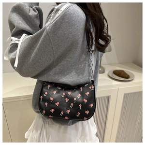 Close-up of black underarm bag with red cherry print and silver chain strap on model