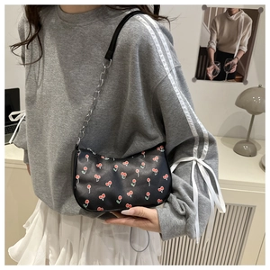 Black half-moon shoulder bag with cherry print and silver chain strap on a model