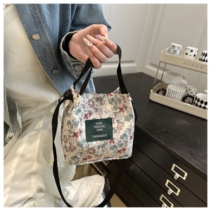 Close-up of floral canvas bucket bag with green label held in a cozy home setting