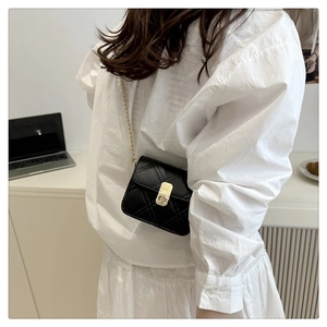Detail of black quilted mini bag featuring golden chain strap and metallic clasp closure