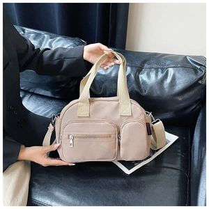 Close-up of beige nylon Boston bag with functional zippers and side logo on a leather sofa