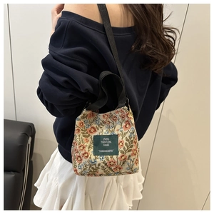 Detail of floral canvas crossbody bag with pattern and brand tag shown on model