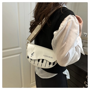 Détail du motif de touches de piano et du texte musical sur un sac besace blanc