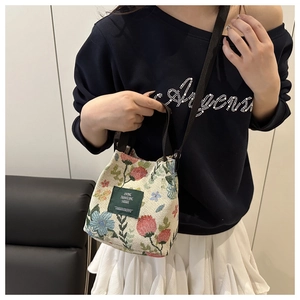 Detail of floral jacquard bucket bag with woven label and adjustable brown shoulder strap