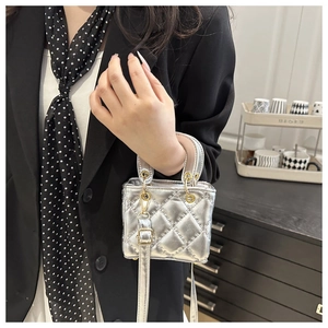 Detail shot of a silver quilted mini handbag featuring gold hardware and a round handle