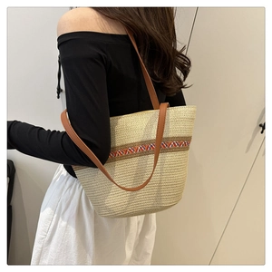 Detail of woven straw bucket bag with colorful ethnic pattern and brown leather straps