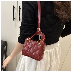 Close-up of red patent leather crossbody bag with quilted texture and gold metal handle