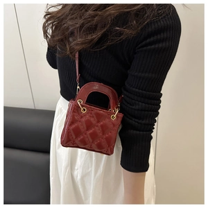 Detail view of burgundy quilted mini bag with patent finish and gold hardware shown on model
