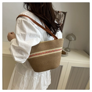 Close-up of a woven straw bucket bag with colorful ethnic pattern trim and leather strap