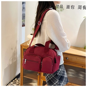 Side view of a burgundy high-density nylon shoulder bag with multi-pocket design on model