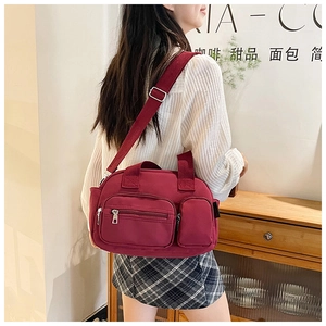 Detail of burgundy multi-pocket crossbody bag showing zippers and wide strap on model