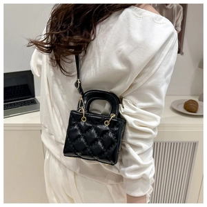 Detail of black quilted mini handbag with gold hardware and adjustable strap in use