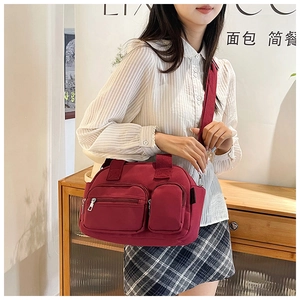 Detailed view of a burgundy shoulder bag with multi-pocket design and wide fabric strap
